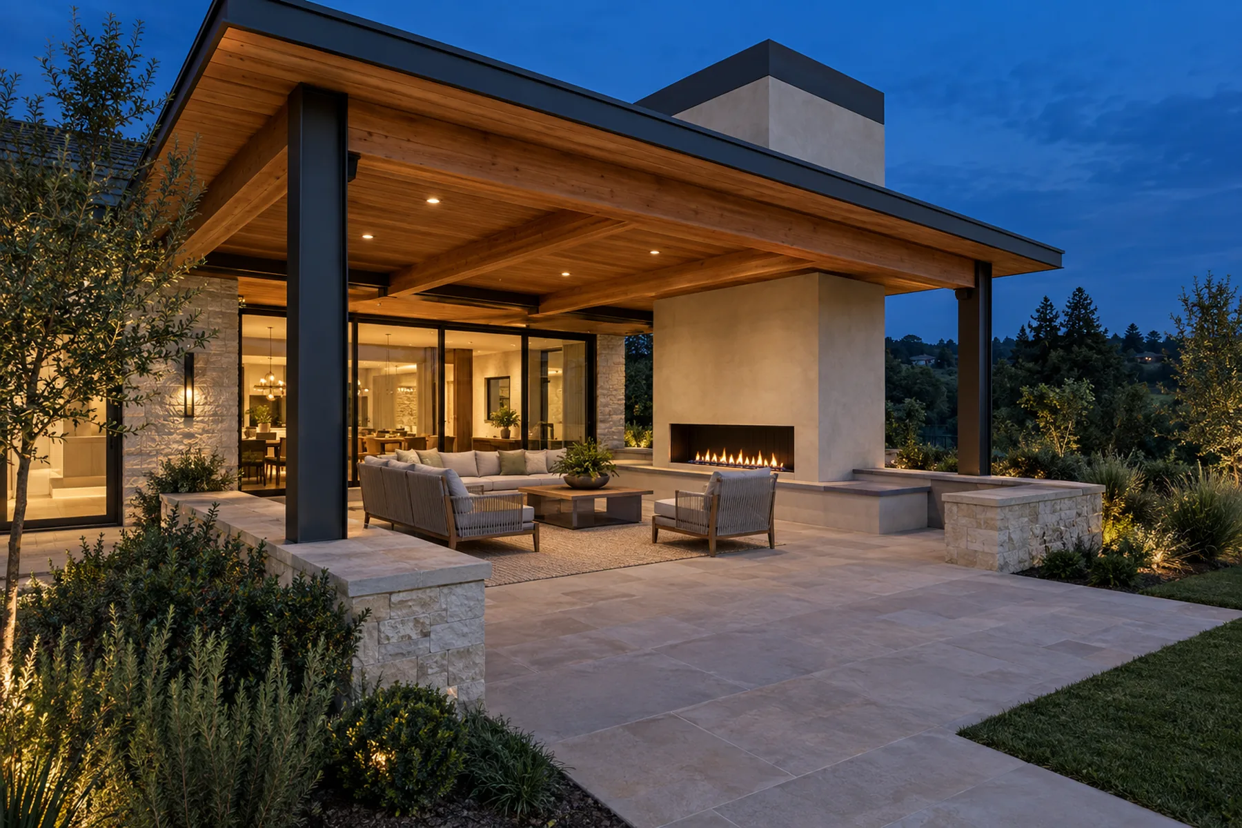Modern covered patio with cedar ceiling, linear fireplace, stone paving and low seat walls at dusk